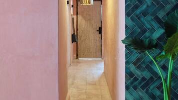 A hallway with a tiled floor, a door at the end, and a potted plant on the right.