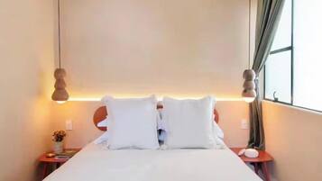 A hotel room with a bed, bedside tables, a lamp, and a window with curtains.