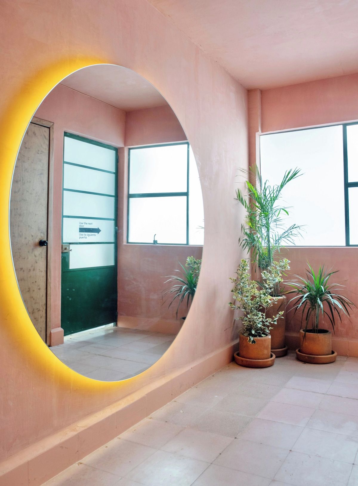 Quarto com espelho grande, plantas em vasos e porta com placa.