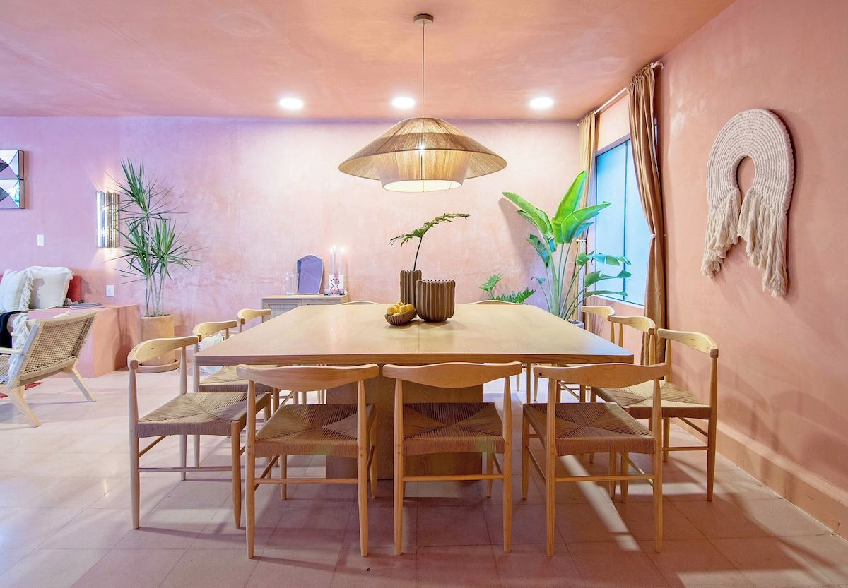 A dining area with a round table, wooden chairs, and a hanging light fixture.