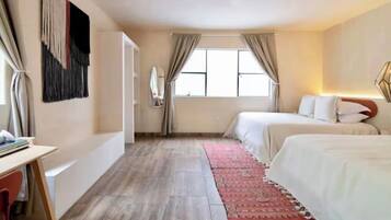 Ein Hotelzimmer mit Bett, Schreibtisch, Stuhl, einem Fenster mit Vorhängen und einem an der Wand hängenden Kunstwerk.