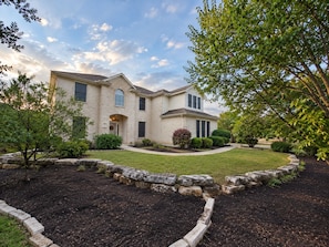 A two-story house with a brick facade, a front porch, and a landscaped yard with a stone border. - Spacious 4-bedroom house with amazing Rock  Pool and massive backyard in Leander (Leander)