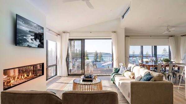 Un salón amplio con chimenea, un sofá y un comedor con vistas al mar.