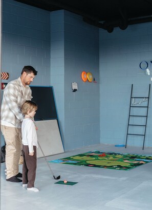 A man and a child playing golf indoors with a mat and a golf ball on a tee.