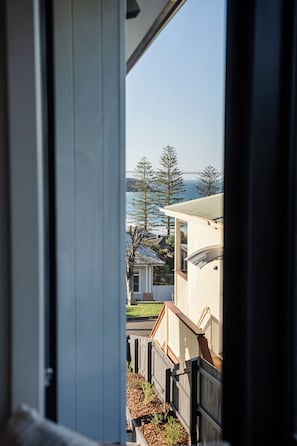 A view through a window with a view of a residential area, including houses and a body of water. - 4BR Ocean Views | Firepit, Games, Pets & Fast WiFi (Black Head)