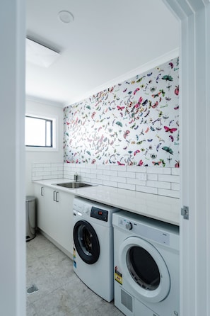 Een wasserette met een witte betegelde spatwand met een motief van vlinders, een wastafel en twee voorladers wasmachines.