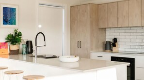 A modern kitchen with a white countertop, wooden cabinets, a sink, and a dishwasher.