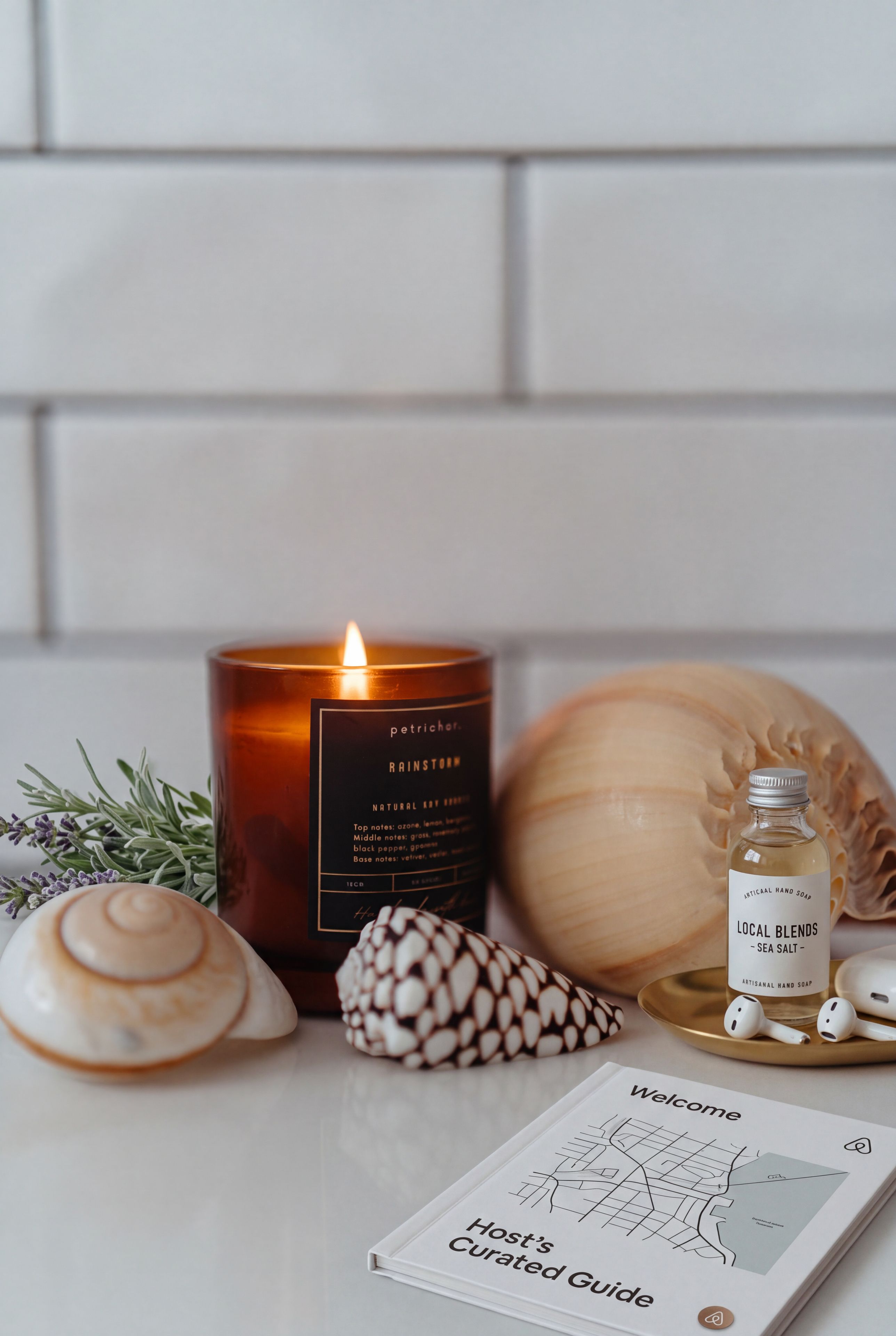 A candle, a bottle of hand soap, a seashell, a wooden object, and a guidebook on a table.