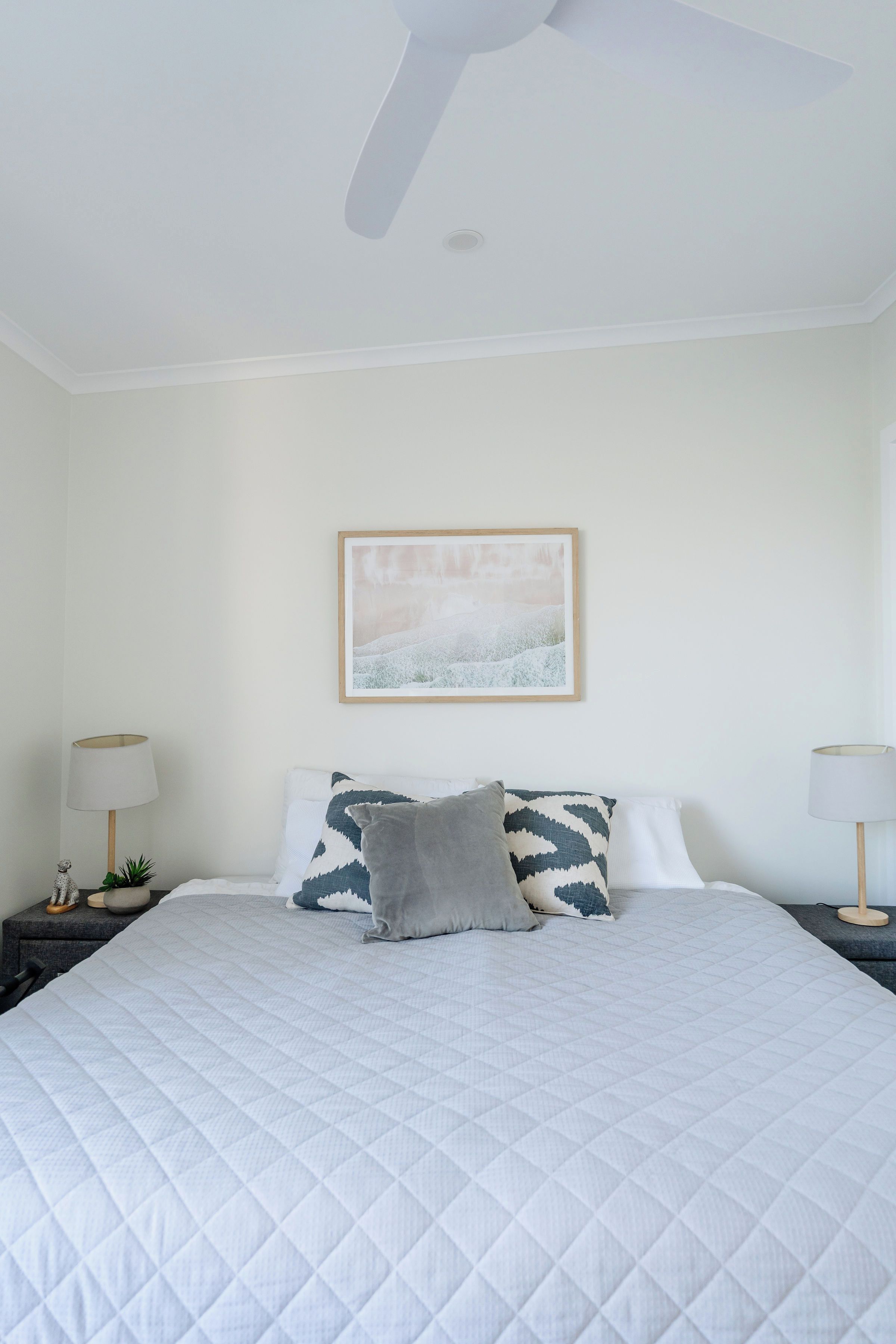 Une chambre à coucher avec un lit, un ventilateur de plafond, un tableau accroché au mur et des lampes de chevet.