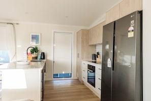 A modern kitchen with a stainless steel refrigerator, wooden cabinets, and a built-in oven. - 4BR Ocean Views | Firepit, Games, Pets & Fast WiFi (Black Head)