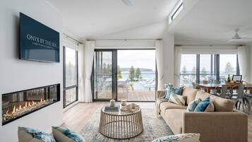 A modern living room with a fireplace, a television, and a view of the sea.