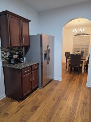 A kitchen with wooden cabinets, a stainless steel refrigerator, a granite countertop, and a dining area with a chandelier. - Charming 3-bedroom house with AC in Rosharon (Rosharon)