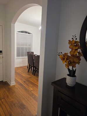A hallway with wooden flooring, a dining area with chairs and a table, and a potted plant on a console table. - Charming 3-bedroom house with AC in Rosharon (Rosharon)