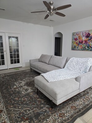A living room with a grey sofa, a patterned rug, a ceiling fan, and a colorful painting on the wall. - Charming 3-bedroom house with AC in Rosharon (Rosharon)