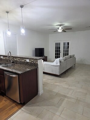 A modern kitchen with granite countertops, a dishwasher, and a built-in oven. There is a dining area with a white sofa and a ceiling fan. - Charming 3-bedroom house with AC in Rosharon (Rosharon)