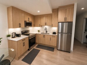 A modern kitchen with wooden cabinets, stainless steel appliances, and a glass dining table. - The Bowness Haven (Calgary)