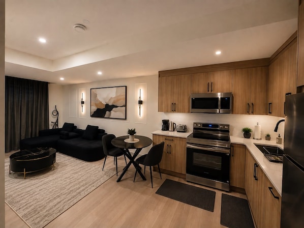 A modern kitchen with wooden cabinets, stainless steel appliances, and a dining area with a black sofa and a small round table.