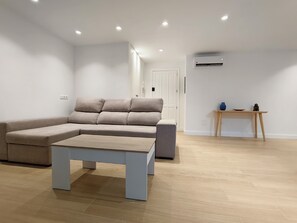 A modern living room with a sectional sofa, a coffee table, and a wooden side table with decorative items. - SAN DIEGO APARTMENT (San Bartolomé de Tirajana)