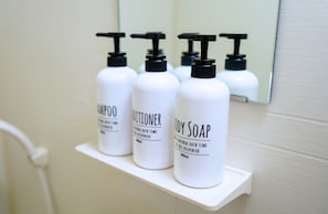 Trois bouteilles de shampoing, d’après-shampoing et de savon pour le corps, posées sur une étagère blanche.
