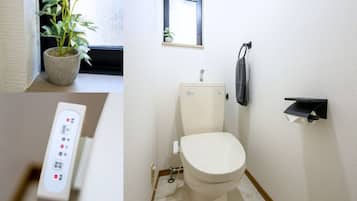 A bathroom with a toilet, a small window, a potted plant, and a control panel.