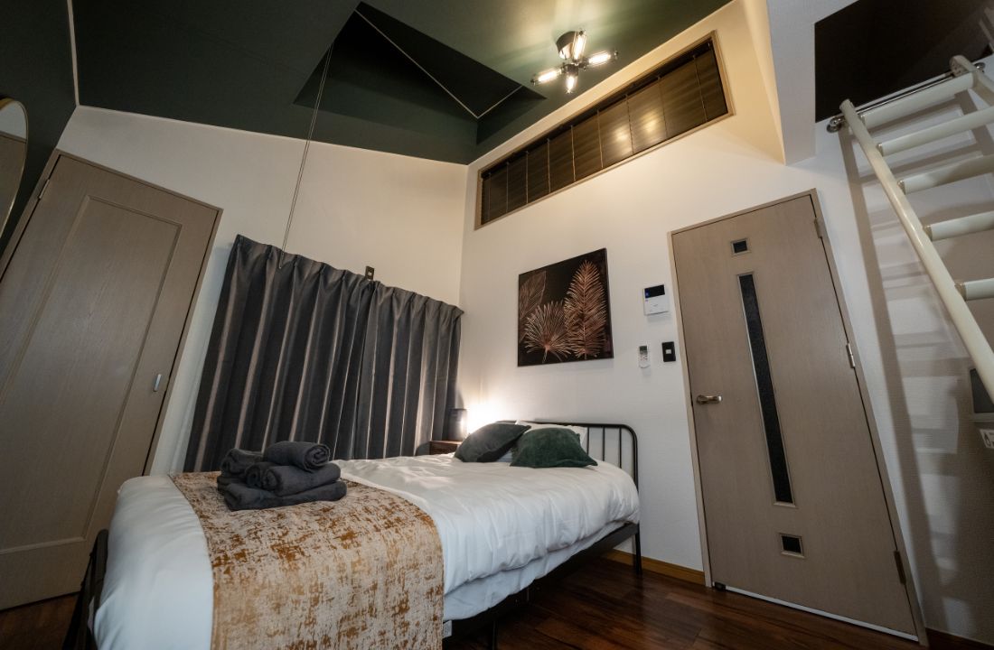 A bedroom with a bed, a window with curtains, a door, and a staircase.