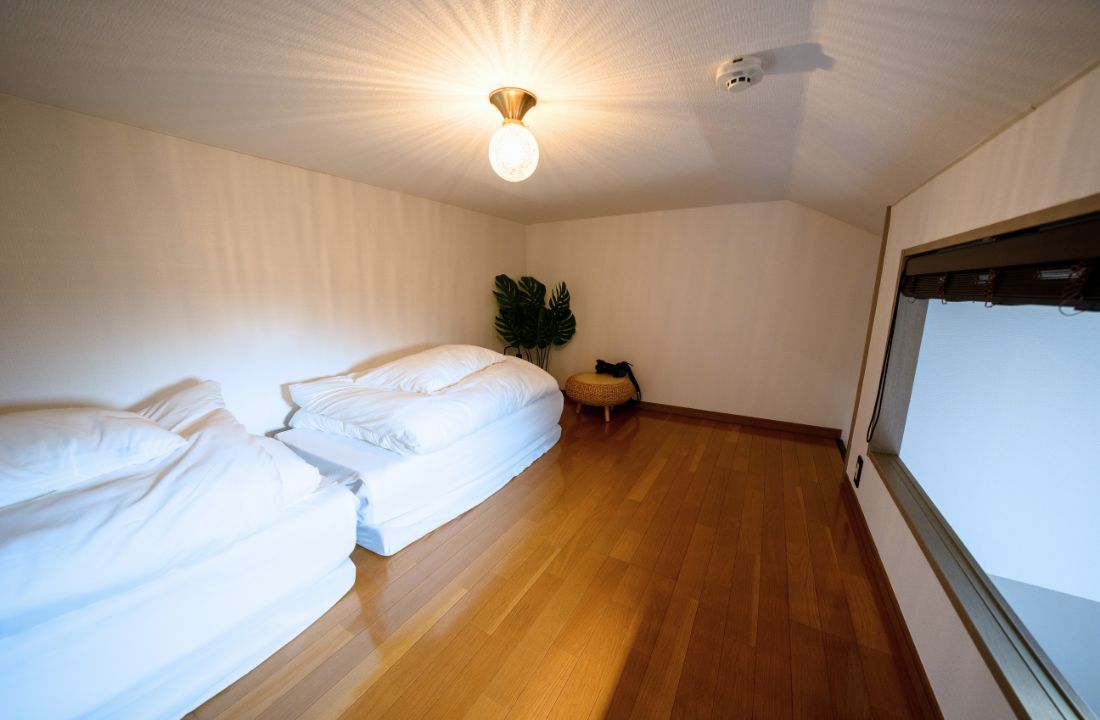 A room with two beds, a ceiling light, a window, and a plant.