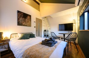 Habitación de hotel con cama, escritorio, silla, televisor y escalera.