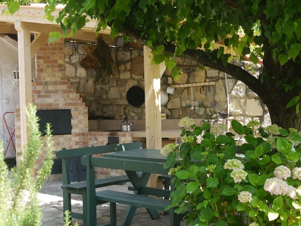 An outdoor kitchen area with a brick oven, wooden benches, and hanging utensils. - Cottage in Szigliget With Swimming Pool (Szigliget)