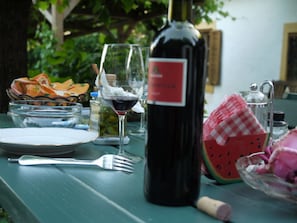A dining table with a bottle of wine, glasses, cutlery, and a watermelon slice. - Cottage in Szigliget With Swimming Pool (Szigliget)