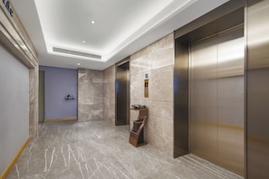 A modern elevator area with marble flooring, a blue wall, and a digital information display. - Kyliab Hotel (Guangzhou)