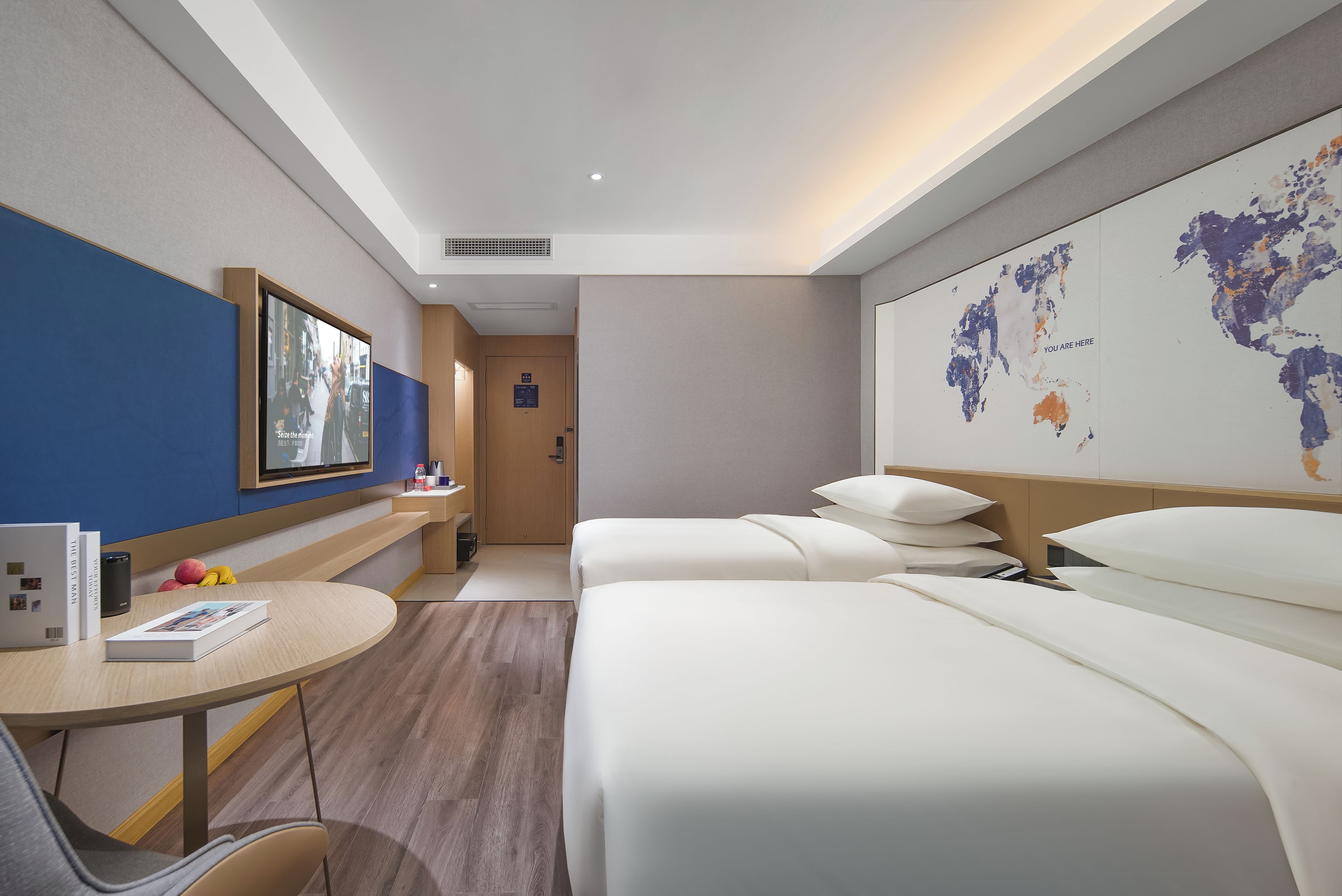 Una habitación de hotel con cama, escritorio con silla, televisión y un mapa mundial en la pared.