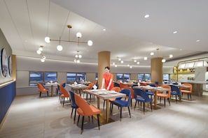 A modern dining area with multiple tables and chairs, a central pillar, and a person standing. - Kyliab Hotel (Guangzhou)