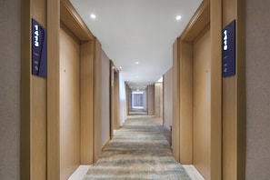 Un pasillo de hotel con paneles de madera, piso alfombrado y números de habitaciones iluminados en las paredes.