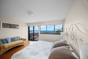 Ein Schlafzimmer mit einem großen Bett, einer Couch, Blick auf das Meer und einem Balkon.