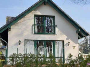 Ein zweistöckiges Haus mit einem grünen Dach, einem Balkon mit Geländer und einem großen Fenster.