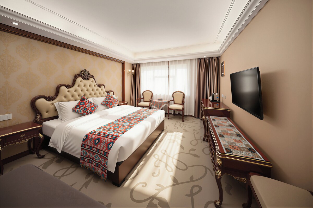 A hotel room with a large bed, two chairs, a desk, and a flat-screen TV.