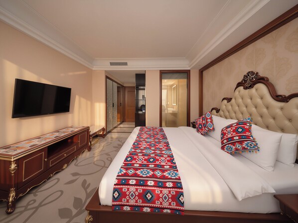 A hotel room with a large bed, a flat-screen TV, a wooden bench, and a walk-in closet.