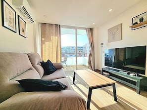 Ein modernes Wohnzimmer mit Sofa, Couchtisch, Flachbildfernseher und einem Balkon mit Blick auf Gebäude.