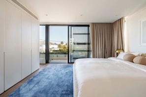 A bedroom with a large bed, a blue carpet, a sliding glass door to a balcony, and a view of buildings outside. - Vogue House, Dover Heights (Dover Heights)