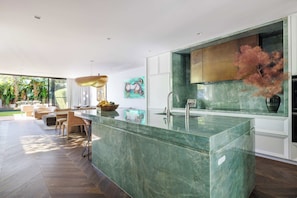 A modern kitchen with a central island, a dining area with a sofa and chairs, and a view of the outdoors. - Vogue House, Dover Heights (Dover Heights)