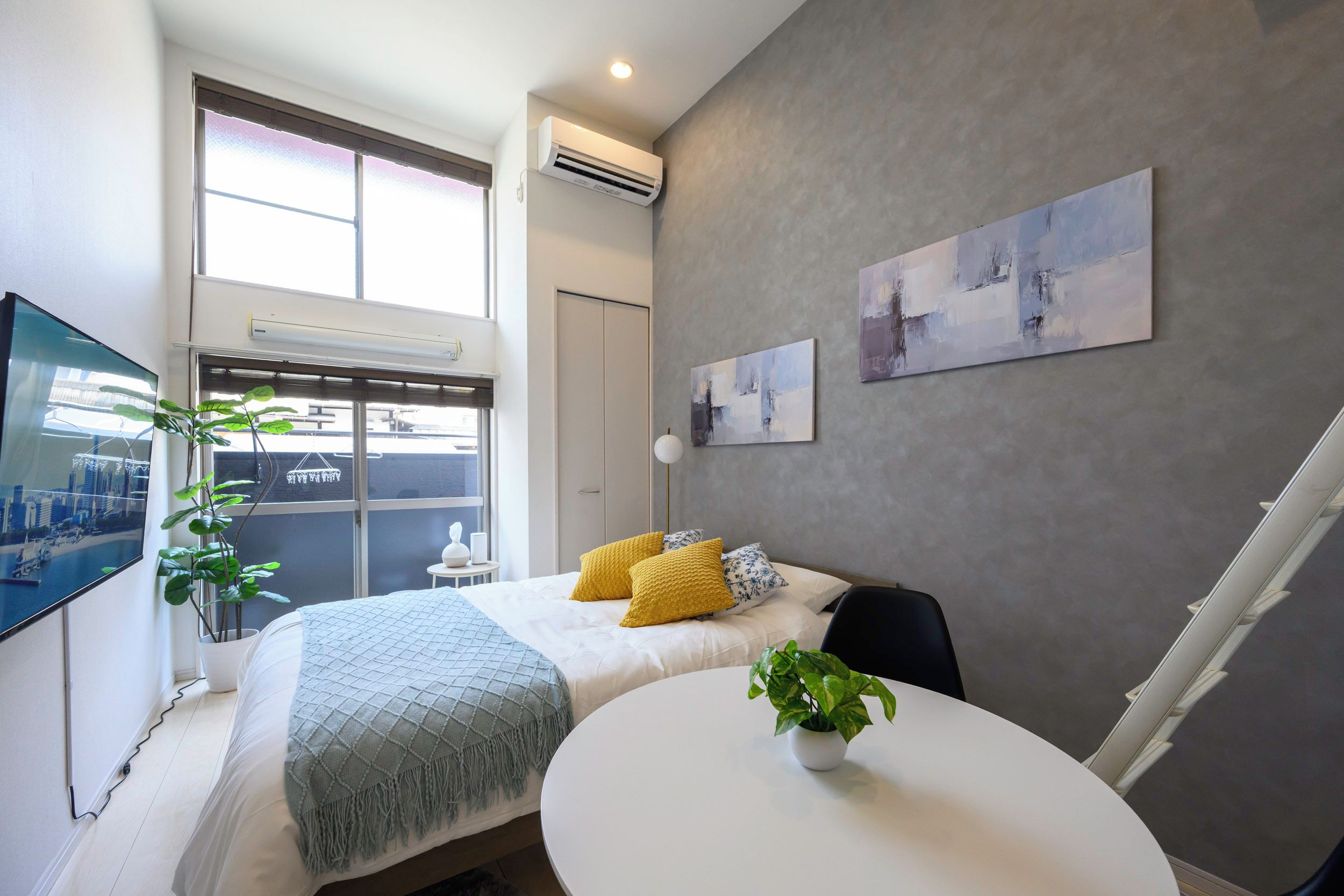 A modern bedroom with a bed, a round table, and a TV on the wall.