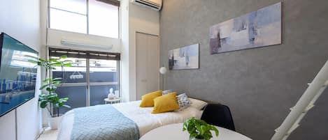 Un dormitorio moderno con una cama, una mesa redonda y un televisor en la pared.