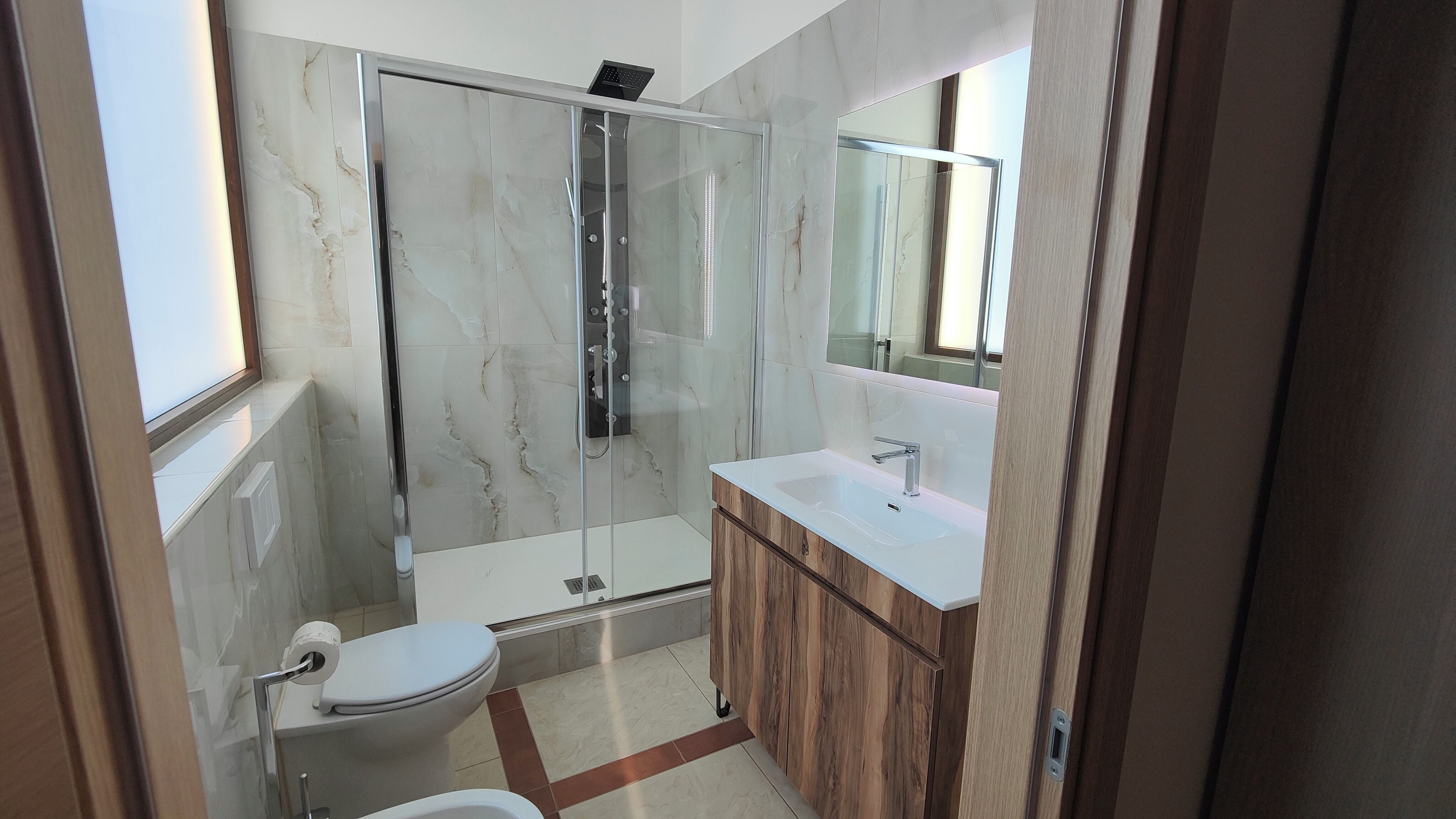 Un bagno moderno con doccia vetrata, un water e un mobile lavabo con specchio.