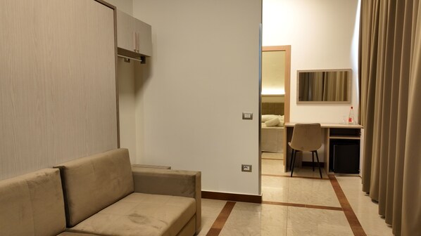 Una habitación de hotel con sofá, escritorio, silla, cama y espejo.
