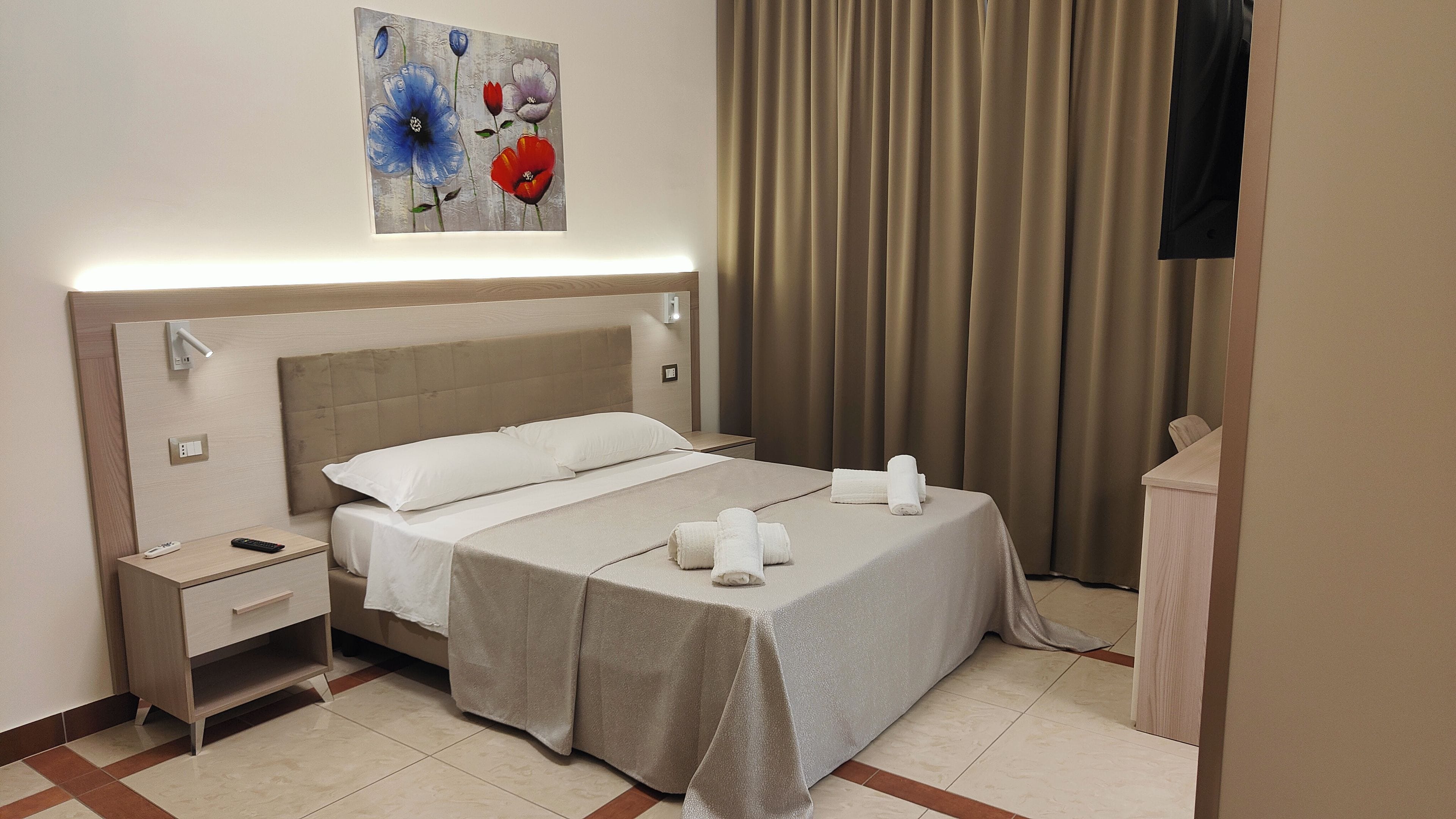 A hotel room with a bed, bedside tables, a painting, and a curtain.