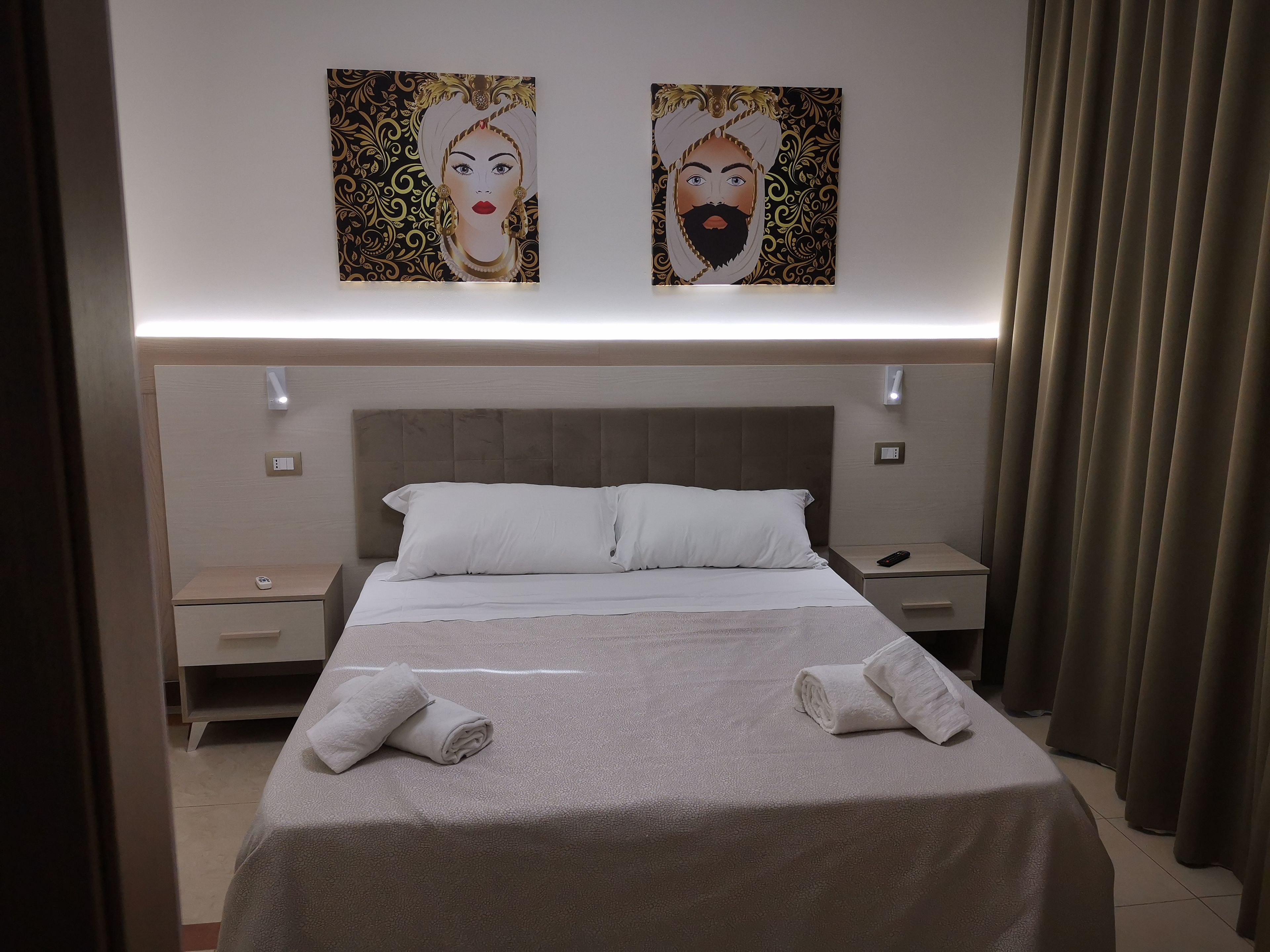 Una habitación de hotel con una cama grande, dos mesitas de noche, una lámpara de pared y una cortina.
