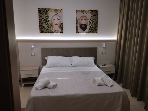 A hotel room with a large bed, two nightstands, a wall-mounted light, and a curtain.