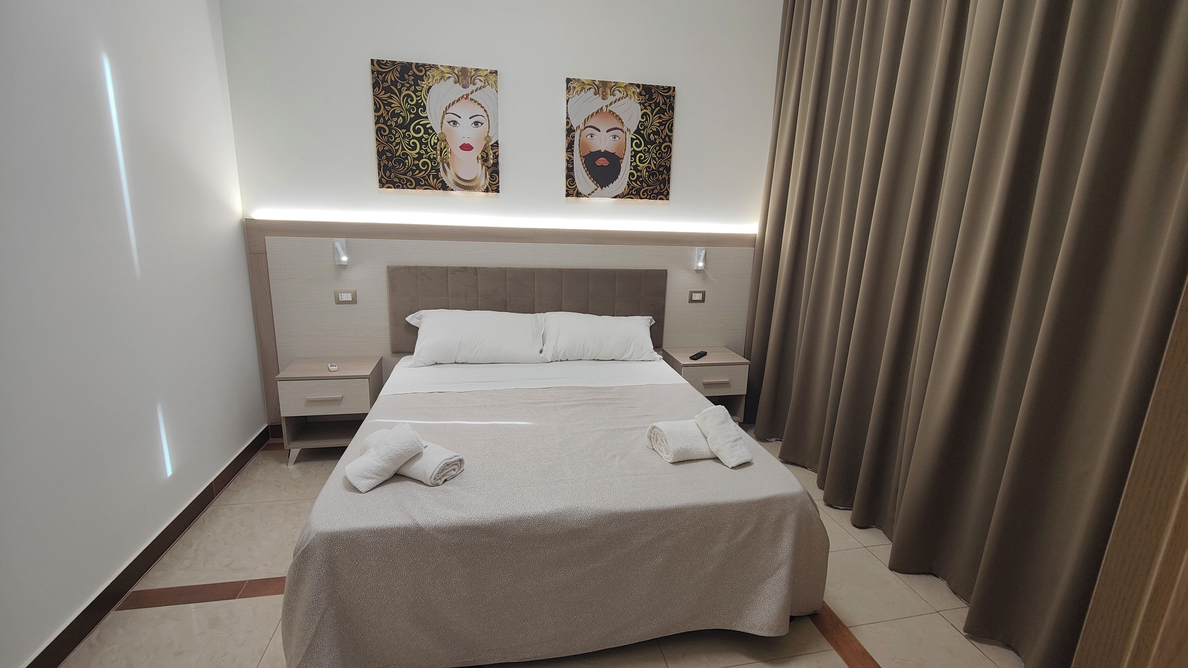 A hotel room with a bed, two nightstands, a headboard, and two wall-mounted artworks.