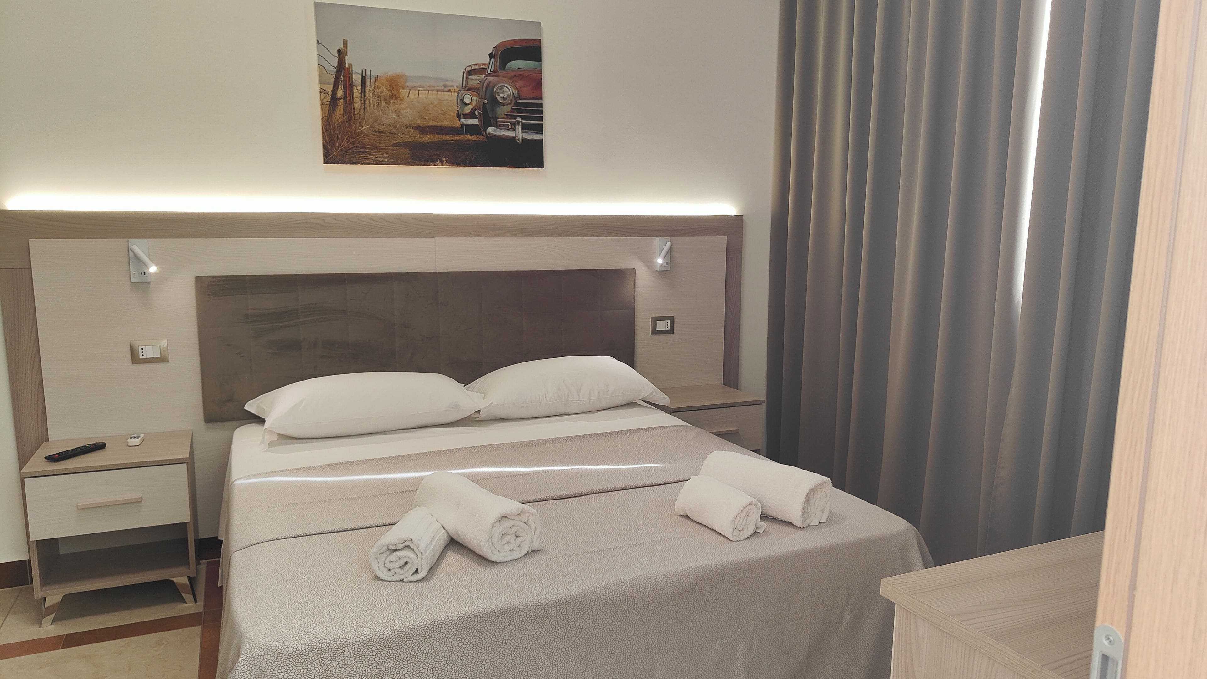 A hotel room with a bed, a nightstand, a remote control, and a painting on the wall.