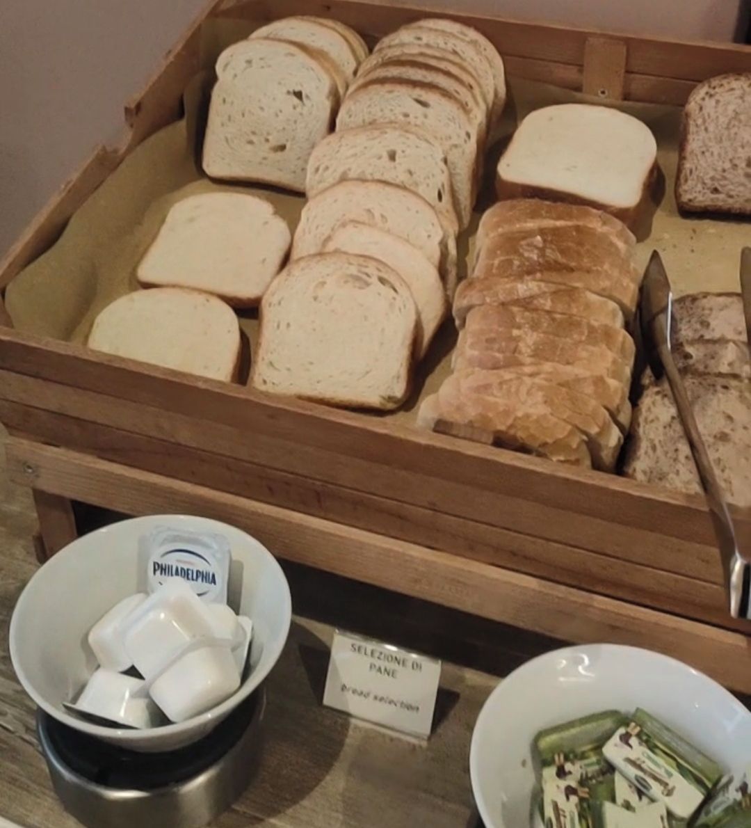 Ein Holzbrotkorb mit verschiedenen Brotsorten und einem Schild, das auf eine Brotauswahl hinweist.